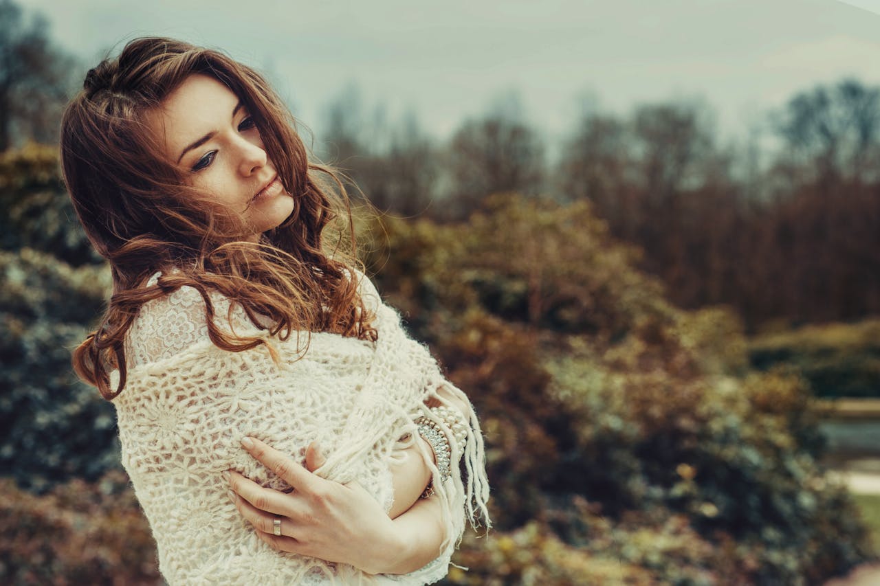 A serene portrait of a woman wrapped in a crochet shawl set against a blurred autumn landscape.