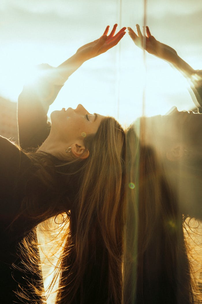 A woman poses gracefully with eyes closed, reflecting sunlight in a serene setting.