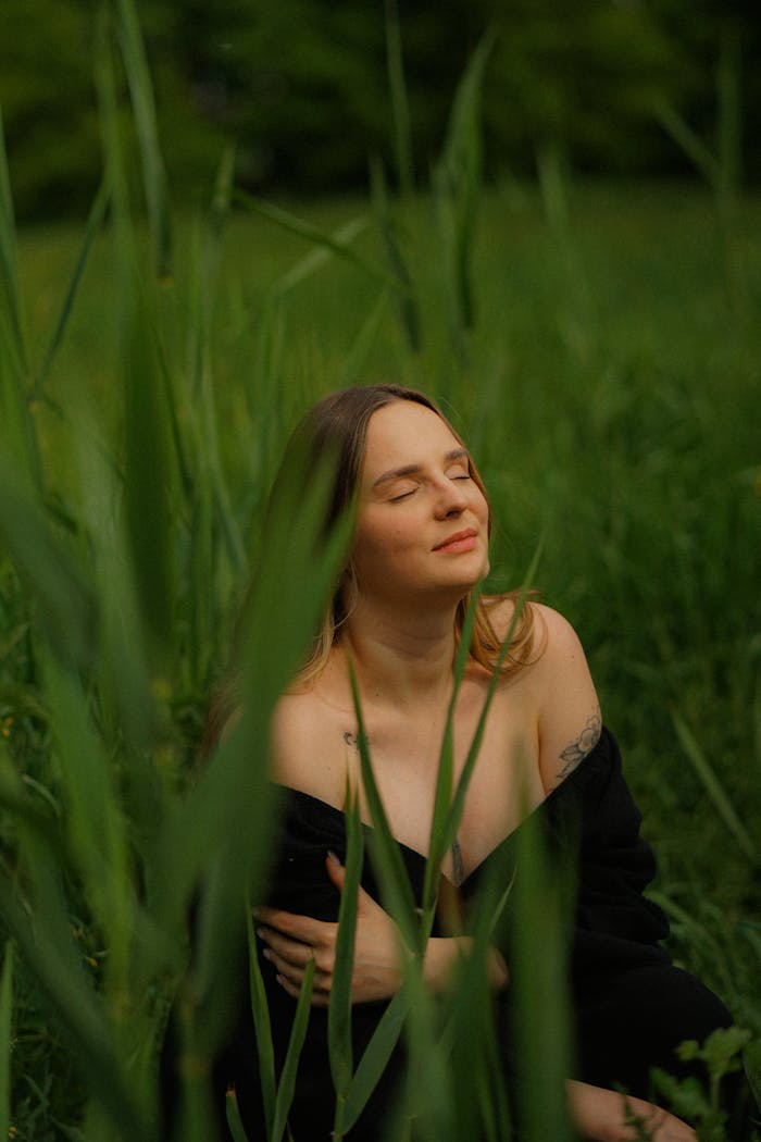 A woman in a black dress enjoys a quiet moment in a lush green meadow during springtime.